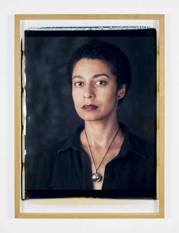 Large format Polaroid self-portrait of a striking looking woman with black short hard, black blouse and necklace