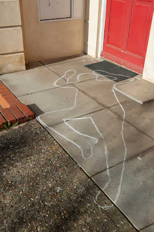 A photo showing the front of a house with a chalk outline of a person drawn on the ground outside the front door. 