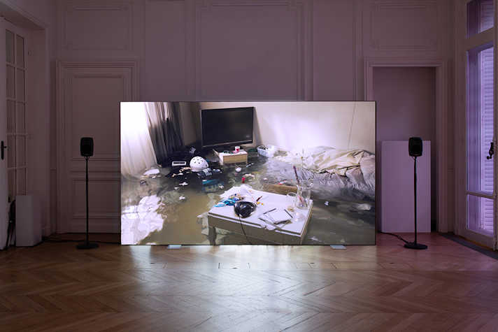 A room large room with wooden floors. In the centre is a large screen with a black speaker on either side. On the screen is an image of a bedroom partially submerged under water.