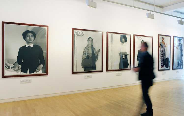 blurred image of a woman in a gallery looking at very large framed portraits of black women.